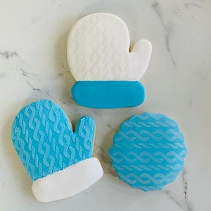 May include: Three blue and white sugar cookies decorated with a knit pattern. The cookies are shaped like mittens and a circle.