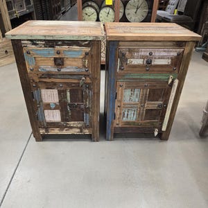 May include: Two rustic wooden nightstands with a distressed, multi-colored patchwork design. Each nightstand features a drawer, a cabinet door, and metal hardware. The nightstands are made of reclaimed wood and have a weathered appearance.