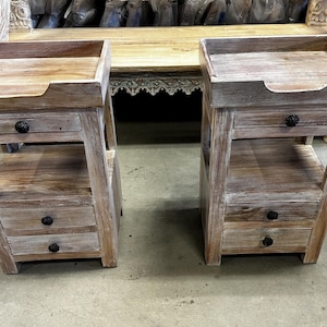 May include: Two rustic wooden nightstands with a distressed finish. Each nightstand has a tray top, a drawer with a black knob, an open shelf, and two additional drawers with black knobs. The nightstands are made of light brown wood.