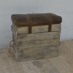 May include: A wooden storage box with a brown leather top and rope handles. The box has a distressed white paint finish and is perfect for storing items or using as a seat.