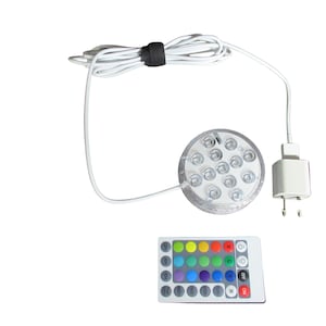 May include: A clear, circular LED light with multiple bulbs, a white power cord, and a remote control with color options. The remote has buttons for various colors and settings. The light is designed for underwater use.
