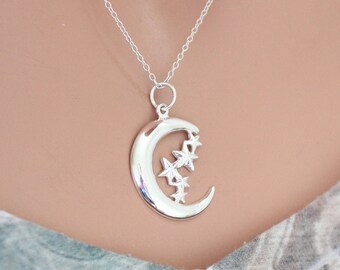Puede incluir: Un collar de plata con un colgante de media luna con pequeñas estrellas. El colgante es un diseño simple y elegante.