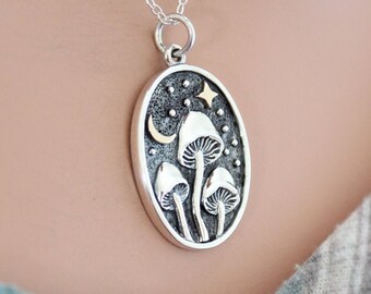 May include: A silver necklace with an oval pendant featuring a crescent moon, a star, and three mushrooms against a black background with white dots.
