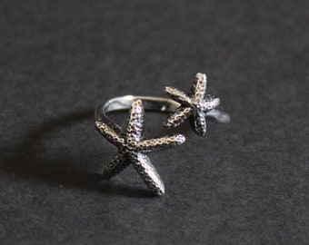 May include: A silver ring with two starfish designs. The starfish are facing opposite directions.