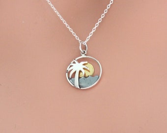 May include: A silver necklace with a circular pendant featuring a palm tree silhouette with a yellow sun behind it.