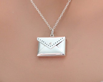 May include: A silver necklace with a small, silver envelope pendant. The envelope has a detailed design and a small, clear stone in the center.