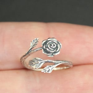 Può includere: Un anello d'argento con un design a forma di rosa. La rosa è avvolta attorno alla fascia dell'anello, con foglie che si estendono dallo stelo.