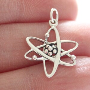 May include: A silver charm in the shape of an atom. The atom has a central nucleus with orbiting electrons.