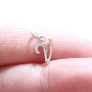 Puede incluir: Un charm de plata en forma de la letra V. El charm es pequeño y delicado, y sería perfecto para agregar un toque personal a un collar o pulsera.