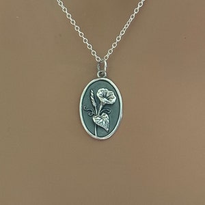 Peut inclure: Un collier en argent avec une cha&icirc;ne d&eacute;licate et un pendentif ovale repr&eacute;sentant une fleur de gloire du matin en argent d&eacute;taill&eacute;e.