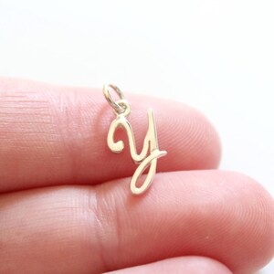 May include: A silver charm in the shape of the letter Y. The charm is in a cursive font and is being held by a finger.