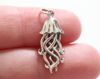 May include: A silver charm in the shape of a jellyfish with intricate details. The charm is designed with a detailed, knotted body and a bell-shaped head.