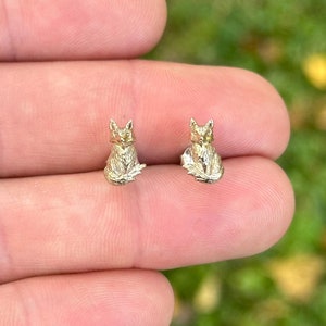 May include: A pair of gold fox stud earrings. The fox is sitting with its tail curled around its body.
