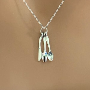 May include: A silver necklace with a charm of a knife, fork, and spoon hanging from it.
