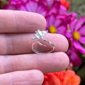 Puede incluir: Un anillo de plata con un diseño de manta raya. El anillo es ajustable y tiene un acabado liso y pulido.