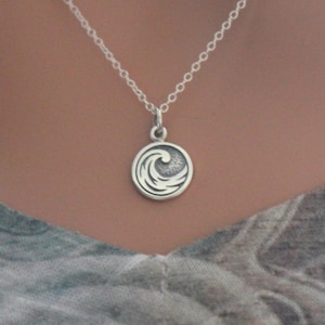 May include: A silver necklace with a small, round pendant featuring a stylized wave design.