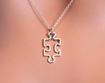 Puede incluir: Un collar de plata con un colgante de pieza de rompecabezas. El colgante es un simple contorno de una pieza de rompecabezas.