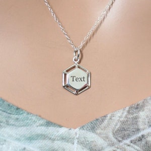 May include: A silver necklace with a hexagonal pendant that has the word "Text" engraved on it.