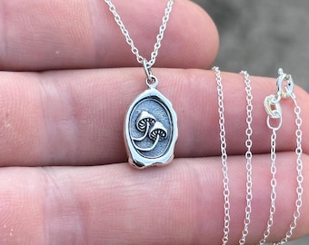 May include: A silver necklace with a pendant featuring two mushrooms in a wax seal design.