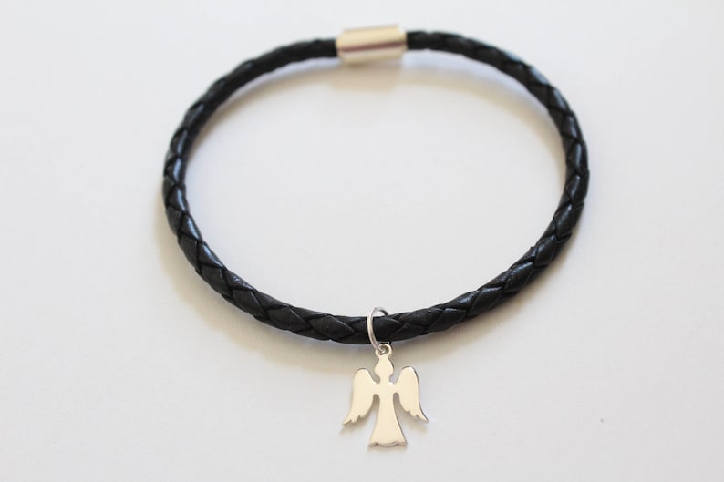 Puede incluir: Un brazalete trenzado de cuero negro con un dije de &aacute;ngel de plata.