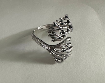 Puede incluir: Un anillo de plata con un diseño de rama de árbol. El anillo está abierto y tiene un acabado texturizado.