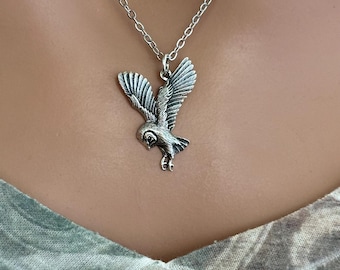 Könnte beinhalten: Halskette mit silberfarbenem Anhänger, der eine fliegende Eule zeigt. Die Eule hat ausgebreitete Flügel und detaillierte Federzeichnungen. Die Kette ist im filigranen Gliederstil gehalten, der Anhänger vor neutralem Hintergrund.