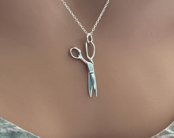 Op de afbeelding: Een zilverkleurige ketting met een kleine schaarhanger. De schaar heeft gedetailleerde open bladen en een lus voor de ketting. De ketting wordt gepresenteerd tegen een neutrale achtergrond, waardoor de sieraden worden benadrukt.