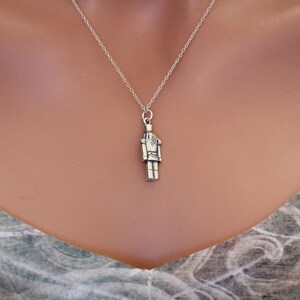 May include: A silver necklace with a nutcracker charm. The charm is detailed and has a classic design.