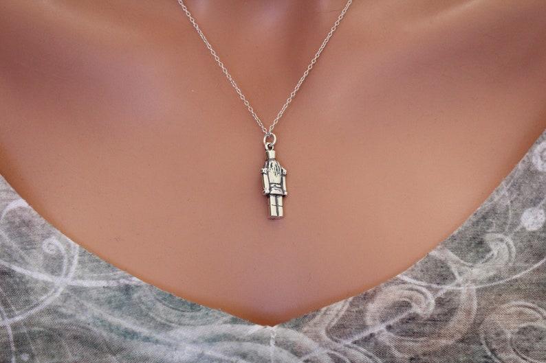 May include: A silver necklace with a nutcracker charm. The charm is detailed and has a classic design.