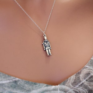 May include: A silver necklace with a detailed nutcracker pendant. The pendant is a traditional nutcracker design with a hat and a mustache.