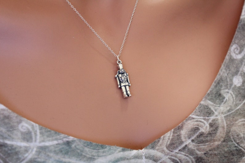May include: A silver necklace with a detailed nutcracker pendant. The pendant is a traditional nutcracker design with a hat and a mustache.