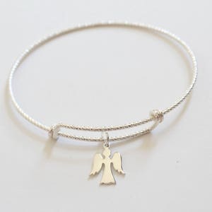 Puede incluir: Un brazalete de plata con un delicado dije de &aacute;ngel. El brazalete est&aacute; hecho de un alambre delgado y trenzado y tiene un dise&ntilde;o simple y elegante.