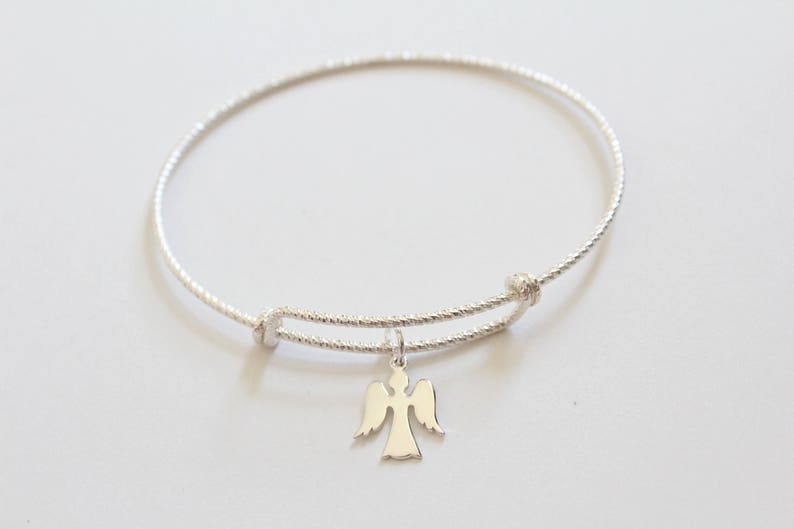 Puede incluir: Un brazalete de plata con un delicado dije de &aacute;ngel. El brazalete est&aacute; hecho de un alambre delgado y trenzado y tiene un dise&ntilde;o simple y elegante.