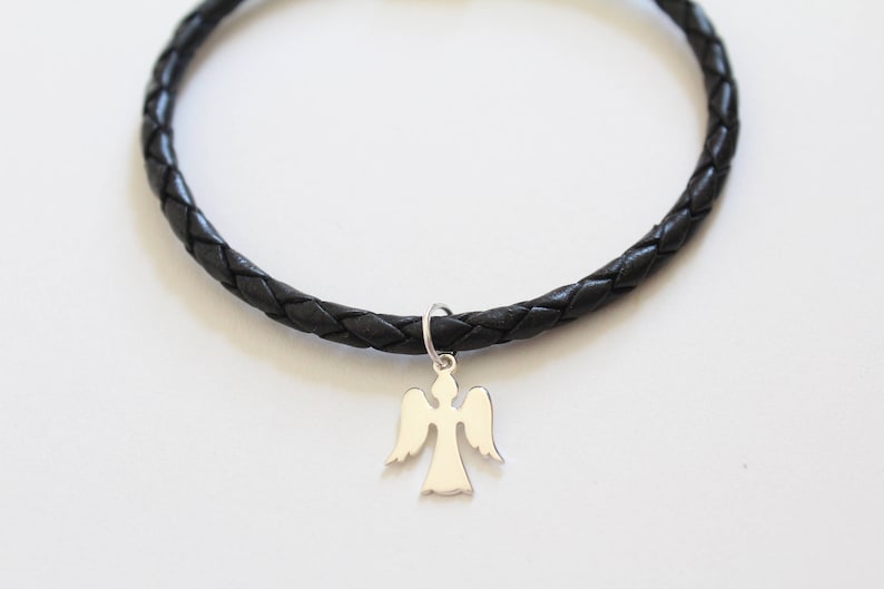 Puede incluir: Un brazalete trenzado de cuero negro con un dije de &aacute;ngel de plata.