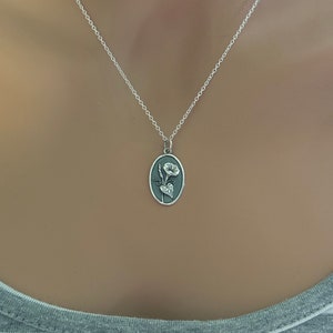 Peut inclure: Un collier en cha&icirc;ne argent avec un pendentif ovale en argent orn&eacute; d'un motif floral grav&eacute;. Le pendentif repr&eacute;sente une fleur stylis&eacute;e avec des feuilles.