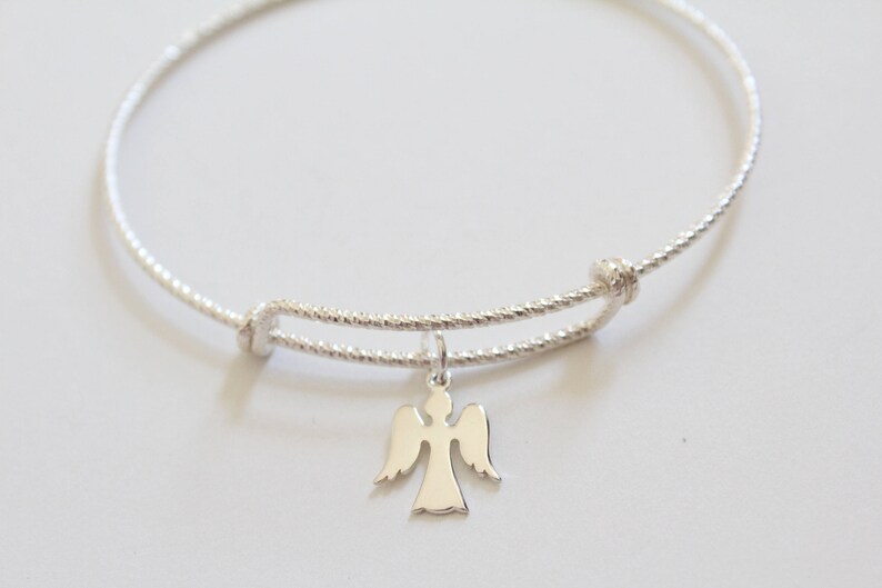 Puede incluir: Un brazalete de plata con un delicado dije de &aacute;ngel. El brazalete est&aacute; hecho de alambre trenzado y tiene un cierre simple.