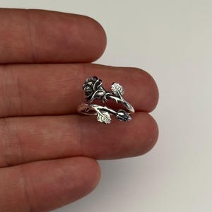 May include: A silver ring with a rose design. The ring is adjustable and features a rose with leaves and a bud.