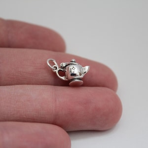 May include: A silver charm in the shape of a teapot with a star on the side.