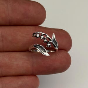 May include: A silver ring with a lily of the valley design. The ring is open and wraps around the finger.