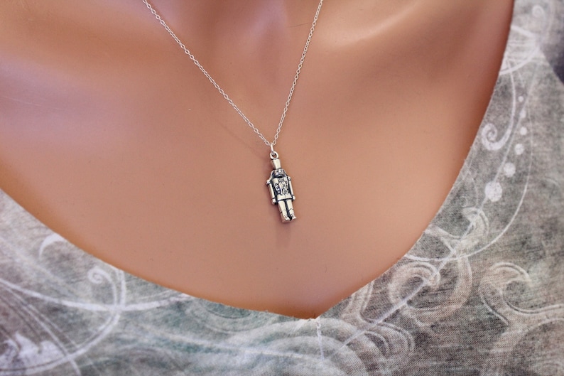 May include: A silver necklace with a detailed nutcracker pendant. The pendant is a small, realistic depiction of a nutcracker soldier.