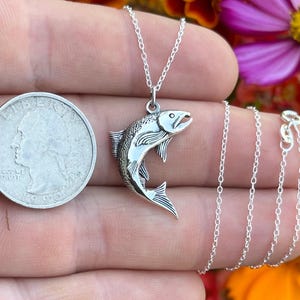 May include: A silver necklace with a detailed silver fish pendant. The pendant is about the size of a quarter. The necklace is on a silver chain.