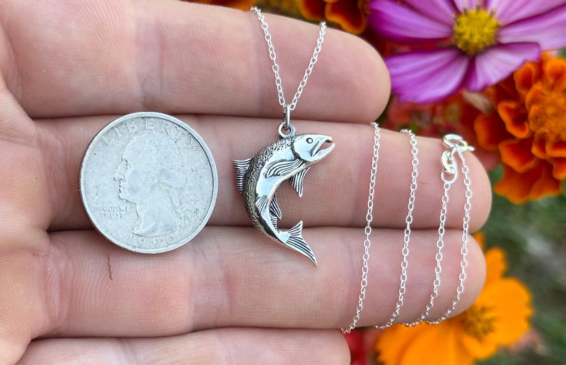 May include: A silver necklace with a detailed silver fish pendant. The pendant is about the size of a quarter. The necklace is on a silver chain.