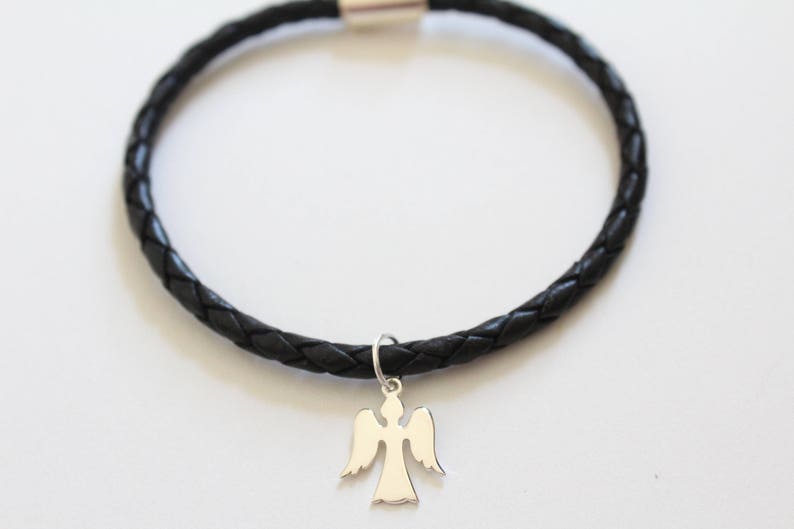 Puede incluir: Un brazalete de cuero trenzado negro con un dije de &aacute;ngel de plata.
