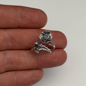 Op de afbeelding: Een zilveren ring met een klaproos-ontwerp. De bloem is gedetailleerd met een stengel en bladeren.