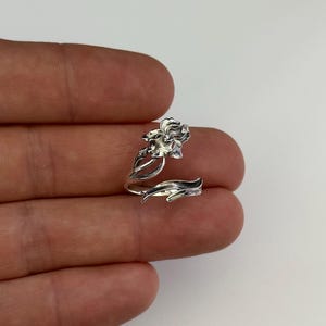 Puede incluir: Un anillo de plata con un diseño de flor de iris detallado. La flor está envuelta alrededor de la banda del anillo.