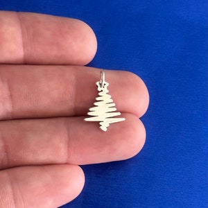 May include: A silver charm in the shape of a Christmas tree. The tree is made of thin, wavy lines.