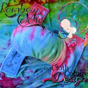 Könnte beinhalten: Eine blaue und pinkfarbene Bindewindel im Tie-Dye-Muster mit den Worten "Rainbow Catcher" und "by Cloth Culture Designs" darauf gedruckt. Die Windel ist gefaltet und liegt auf einem Untergrund aus Tie-Dye-Stoff.