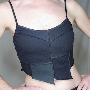 May include: A black crop top with a patchwork design. The top is made of different shades of black fabric and has a raw edge finish.