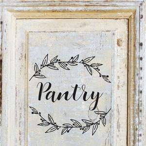 May include: A white wooden cabinet door with a black painted wreath and the word "Pantry" in a cursive font.