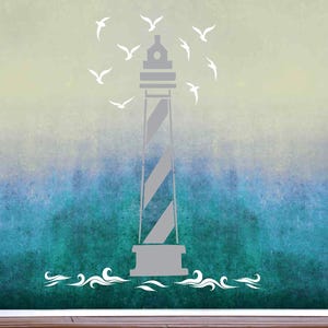 May include: A wall decal featuring a gray lighthouse with diagonal stripes, surrounded by white silhouettes of flying seagulls. The design includes stylized white waves at the base of the lighthouse, set against a gradient background transitioning from light yellow to deep blue.